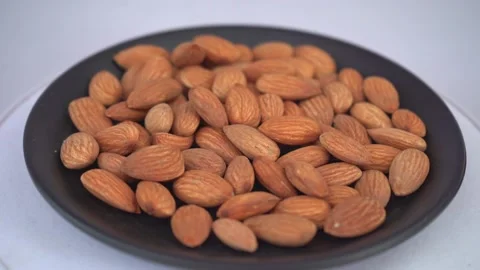Close up fresh almonds in black plate is rotating Stock Footage 294000757