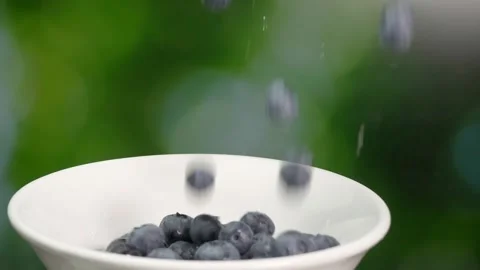 Close-up of fresh blue berry falling on plate on green background. Stock Footage 248791396