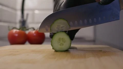 Close-up of a fresh cucumber slice beneath a kitchen knife on a wooden cutting Stock Footage 346858330