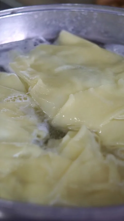 Close-up of fresh dough sheets boiling in hot water inside a metal pot for tradi Stock Footage 342627737