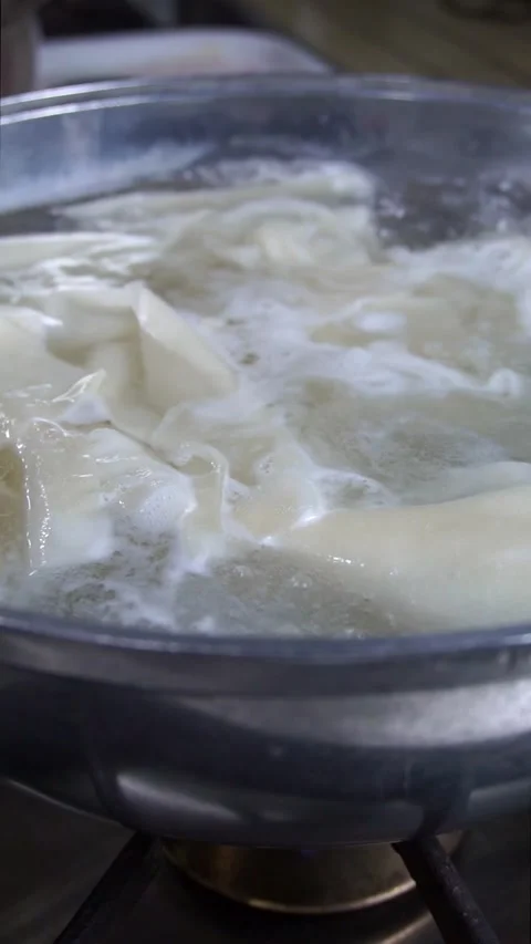 Close-up of fresh dough sheets boiling in hot water inside a metal pot for tradi Stock Footage 342627780