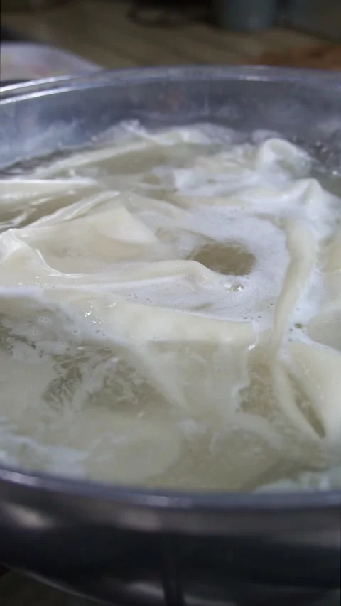 Close-up of fresh dough sheets boiling in hot water inside a metal pot for tradi Stock Footage 342627816