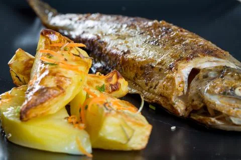 Close up of fresh fried trout with rustic potatoes on a black plate Stock Photos