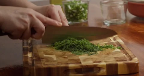 Close-up of fresh herbs being finely chopped on a wooden cutting board on a Vídeos de archivo 327628537