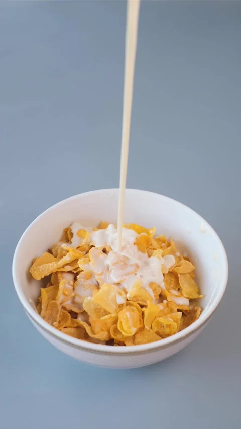 A close-up of fresh milk being poured into a bowl of golden cornflakes Stock Footage 302649679