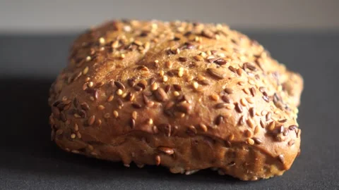Close up of fresh multigrain bread roll on black background studio video Video stock 318844427
