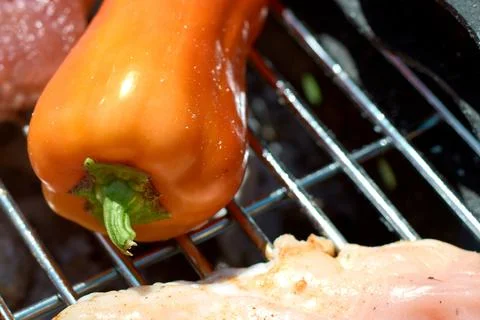 Close-up of a fresh orange pepper grilling on a hot metal barbecue grate Stock Photos