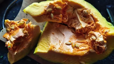 Close-up of Fresh Raw Pumpkin Slices with Seeds on a Wooden Cutting Board Видео 324947105