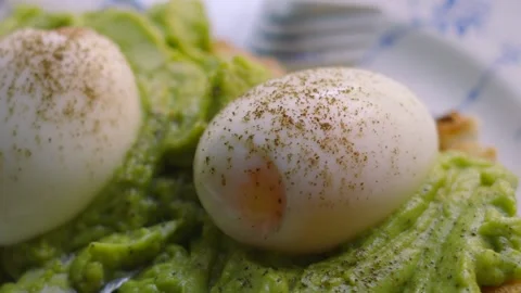 Close-up of Fresh Soft Boiled Eggs with Pepper and Smashed Avocado on Sourdough Stock Footage 342272883