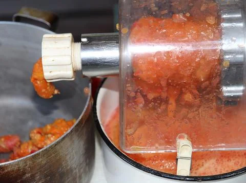 Close-up of fresh tomatoes being processed through a manual food grinder 库存照片