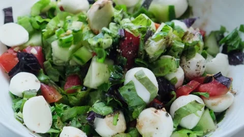 Close-up fresh vegetable salad with mozzarella cheese is stirred with a spoon. Stock Footage 202793100