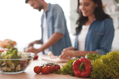 Close up of fresh vegetables on the table with people cooking on the backgrou Stock Photos