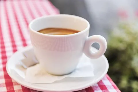 Close-up of a fresh white ceramic cup of hot espresso on checkered tablecloth Stock Photos