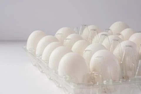 Close-up of fresh white chicken eggs in a clear plastic carton on a white bac Stock Photos