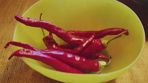 Close up of fresh whole red chilli peppers in a blue plastic bowl on a wooden Stock Footage 273558250