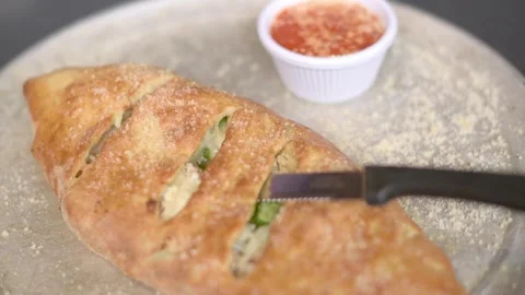 Close-up of a freshly baked calzone being cut, served with marinara sauce Vidéo 277617074