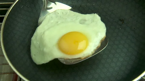 Close-up fried egg removed from frying pan with spatula to a plate with bacon Stock Footage 146884848