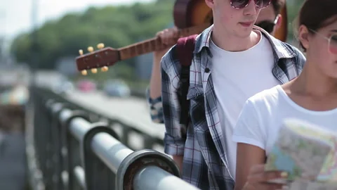 Close up friends walking on viaduct with map and guitar on shoulder, cars Stock Footage 131466363