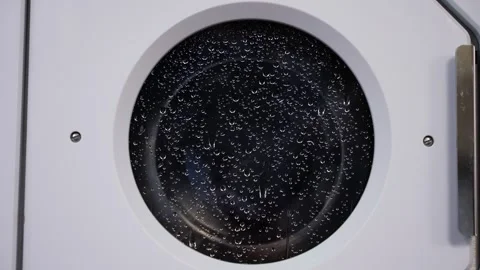 Close-up of a front-loading washing machine door covered with water droplets Video stock 325866517