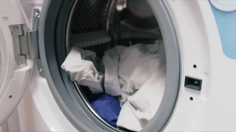 Close up of a front-loading washing machine with colorful clothes being loaded Stock Footage 345080382