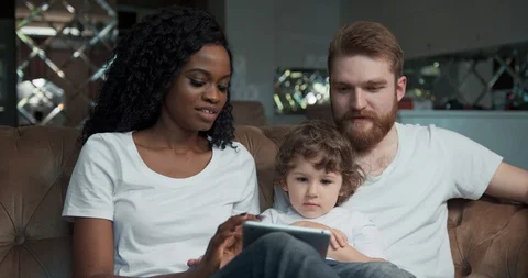 Close-up front view of a happy mixed race couple sitting on a sofa together with Stock Footage 123214263