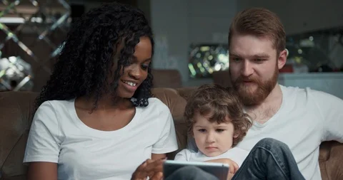 Close-up front view of a happy mixed race couple sitting on a sofa together with Stock Footage 123214350