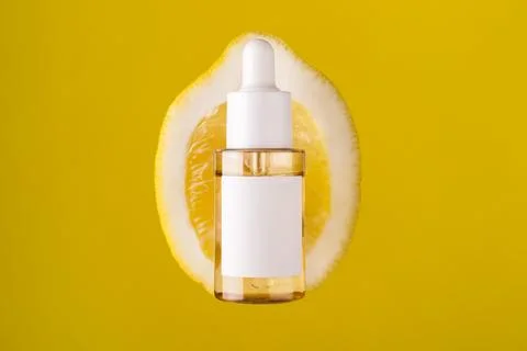 Close up front view of lemon decorated with glass cosmetic serum jar on yel.. Stock Photos