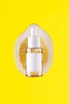 Close up front view of lemon decorated with glass cosmetic serum jar on yel.. Stock Photos