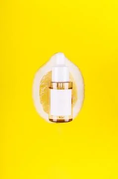 Close up front view of lemon decorated with glass cosmetic serum jar on yel.. Foto stock