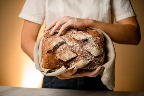 Close-up front view of rustic organic loaf of bread in hands of woman. 스톡 사진