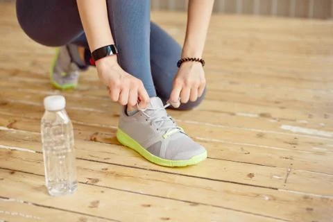 Close-up front view of woman's hands tying shoelaces on sneakers in the gym. Stock Photos