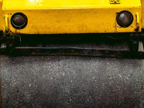 Close Up Front of Yellow Road Roller with Headlights and Asphalt Texture Stock Photos