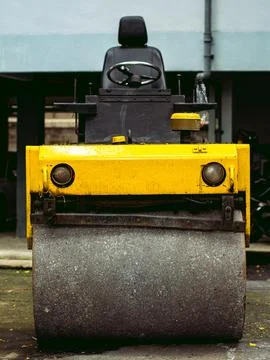 Close Up Front of Yellow Road Roller with Headlights and Asphalt Texture 库存照片