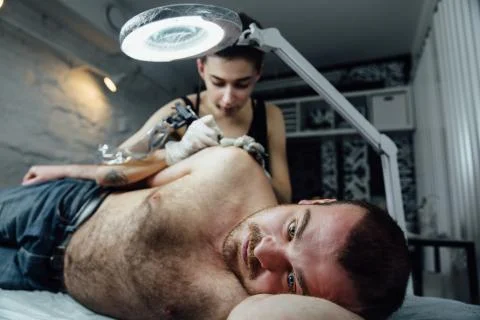 Close frontal portrait of lying man on couch, client of tattoo salon in process Stock Photos