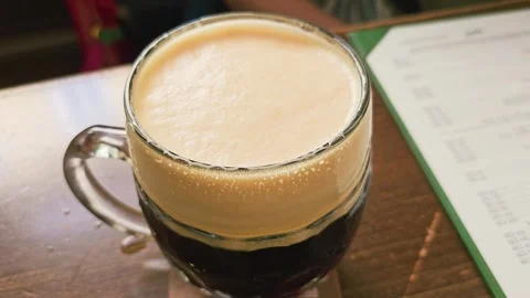 Close-up of a frothy dark beer mug on a wooden pub table, with creamy foam Stock Footage 339235066