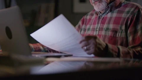 Close up of frustrated older man with paperwork and laptop at night / Cedar Stock Footage 77473106