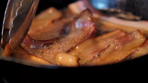 Close-up of frying bacon being flipped with silver tongs. Stock Footage 138333003