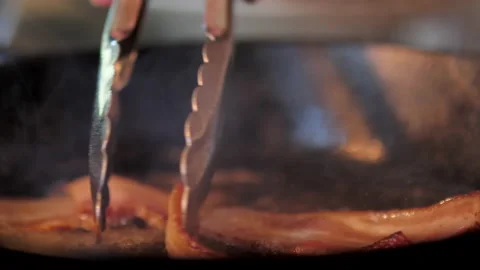 Close-up of frying crispy bacon being moved with silver tongs. Stock Footage 138333006
