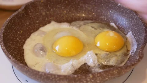 Close-up of frying pan with scrambled eggs into which another egg is broken to Stock Footage 220425496
