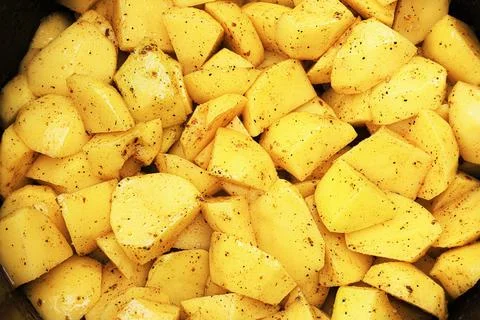 A close-up, full-frame view of raw, diced yellow potatoes seasoned with bla.. Foto stock