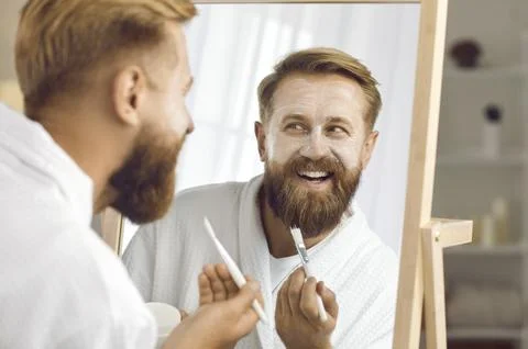 Close up of funny man reflected in mirror who applies cosmetic mask for facial Fotos de archivo