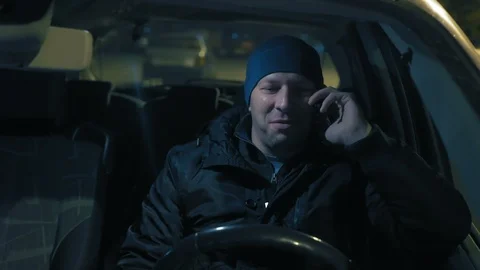 Close-up, Funny Man Talking on the Phone Sitting at the Wheel of a Car at Night Stock Footage 98472968
