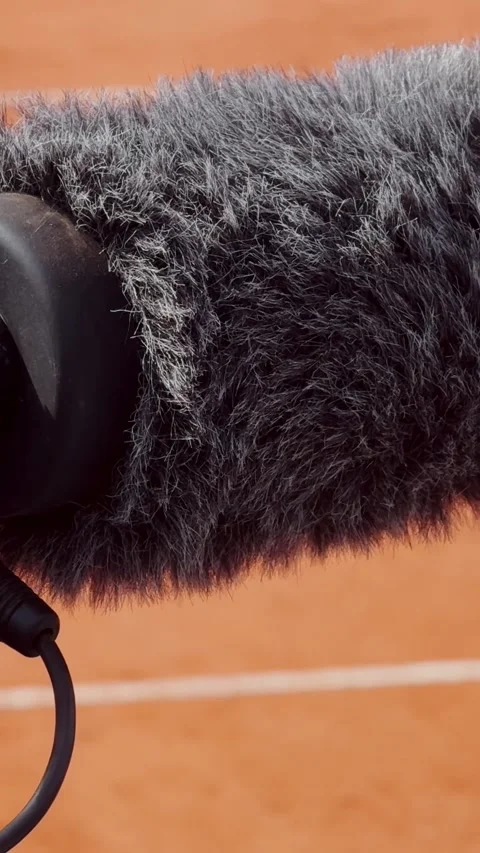 Close-up of a furry camera microphone beside a clay tennis court, showing Stock Footage 337253086