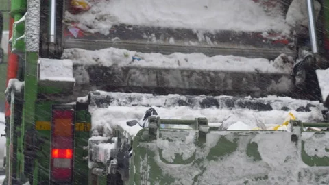 Close-up of a garbage truck automatically dumps garbage cans on a snowy winter d Stock Footage 220618420