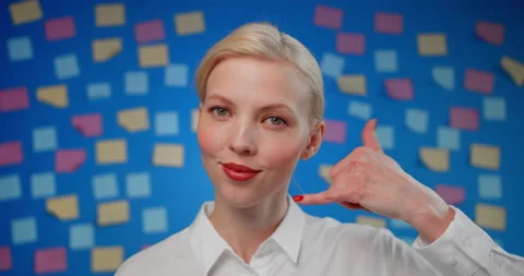 Close-up gesture call us. Beautiful young woman in white shirt looks at camera Stock Footage 151607386