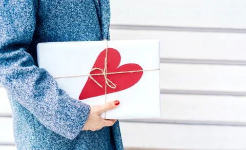Close-up of a gift in paper packaging with a big red heart in female hands. Stock Photos