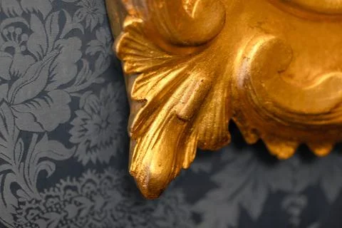 Close-up of a gilded decorative frame corner set against gray damask wallpape 스톡 사진