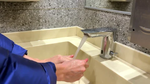 Close-up girl in blue jacket washes her hands in a light yellow wash basin iron Stock Footage 312452896