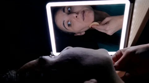 Close-up of a girl in front of the mirror applying make-up on her face Stock Footage 250186508