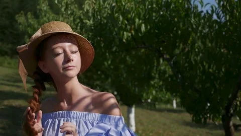 Close-up of a girl in a hat against the background of a peach tree in the garden Stock Footage